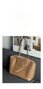 Detail view of a large brown leather tote bag with slender straps on a grey sofa