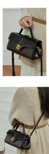 Detail view of the black leather handbag featuring a golden hollow round buckle and strap