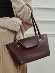 Elegant wine red leather crossbody bag with flap and metal rivets in a lifestyle pose