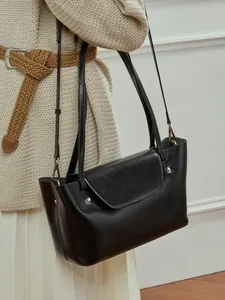Minimalist black leather crossbody bag with metal rivets and shoulder straps on a model