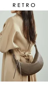 Detailed back view of a minimalist dark brown leather crescent bag on a model in a camel coat