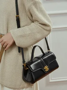 Minimalist black leather top handle bag with gold round clasp shown on a model