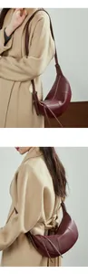 Detail view of burgundy pebble leather croissant bag with sleek tassels and zip closure