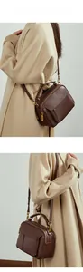 Sac bandoulière en cuir marron foncé porté par un mannequin avec détails dorés