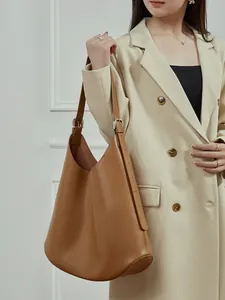 Brown leather tote bag with adjustable strap worn by model in a stylish commuter look