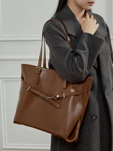Large brown veg-tanned leather tote bag worn by a model with metal buckle detail