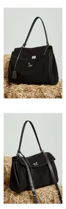 Detail of a large black suede tote bag with silver metal twist lock on a straw background