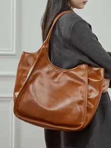 Grand sac cabas en cuir marron porté par un mannequin sur un fond blanc minimaliste