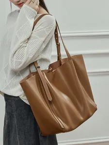 Large tan faux leather tote bag with shoulder strap shown on model against white wall