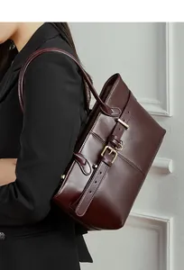 Close-up of leather tote bag with pebble texture, decorative belt, and gold buckle detail