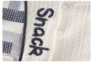 Dettaglio del cardigan in maglia crema per neonato con ricamo Snack e quadri blu