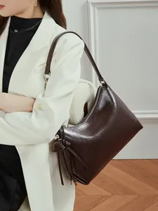 Bolso de hombro de cuero marrón oscuro con borla y detalle de lazo en una modelo