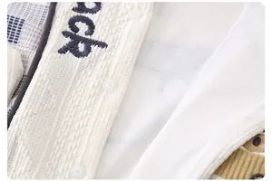 Dettaglio ravvicinato della maglia color crema per neonati con bottoni e ricami blu