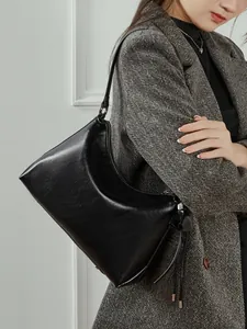 Bolso de hombro minimalista en cuero negro con borlas sobre un abrigo de lana gris