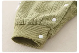 Detail of baby knit romper with green waffle texture, ribbed cuff and white snap buttons