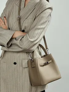 Sac seau en cuir kaki avec fermoir argenté, porté par un mannequin en costume gris