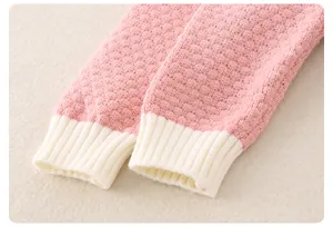 Dettaglio di pagliaccetto in maglia rosa per neonato con polsini a costine bianche