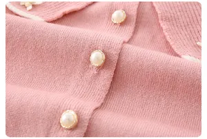 Detail der Baby-Strickjacke mit dekorativen Perlenknöpfen und weißem Kontrastsaum