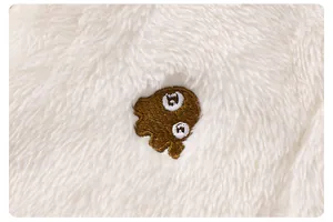 Dettaglio macro del morbido tessuto in pile bianco con una simpatica toppa ricamata marrone