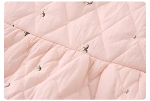 Dettaglio del tessuto trapuntato rosa con ricami a ciliegia per tutine da neonato