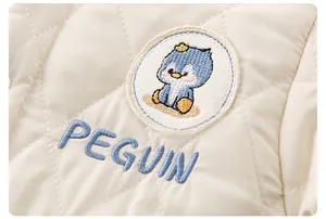 Close-up of quilted baby romper fabric with penguin embroidery and blue letter stitching