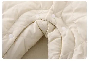 Macro detail of quilted off-white infant romper fabric with durable resin snap buttons