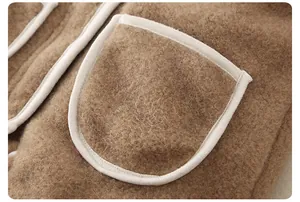 Close-up of thick camel-brown fleece fabric with a large pocket and cream piping trim