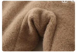 Detail of warm brown plush fabric with soft teddy fleece texture and white embroidery