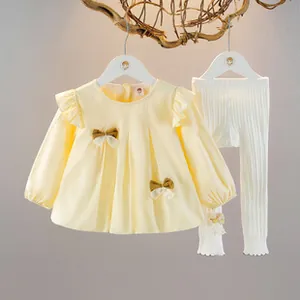 Dettaglio della camicetta gialla con fiocchi e leggings bianchi a coste per bambina