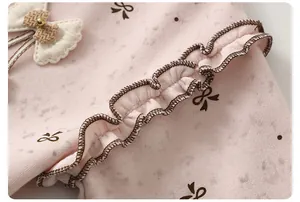 Detail of pink cotton fabric with brown bow prints, ruffles and 3D bow accent