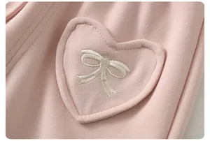 Close-up of pink knit fabric with heart patch and fine white bow embroidery detail