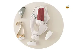Flat lay of baby romper with letter print, wooden toy camera and small bouquet on beige background