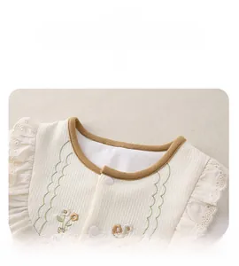Detail von Baby-Strampler mit weißem Waffelstoff, grüner Stickerei und Spitzenbesatz