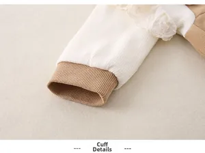 Detail of baby onesie showing white ribbed fabric and brown cuffs with lace trim