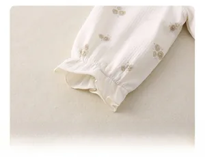 Detailaufnahme von Blumenmuster-Ärmelbündchen mit Rüschenrand an Creme-Baby-Body