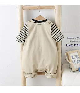 Détail de l'ensemble bébé avec t-shirt rayé et salopette beige sur support bois