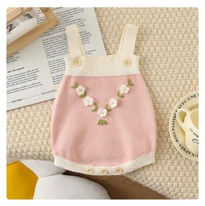 Détail d'une barboteuse en tricot rose avec broderie de fleurs 3D blanches et boutons doux