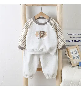Detail von Baby-Baumwoll-Trainingsanzug mit Bären-Patch und Streifenärmeln auf Holzregal