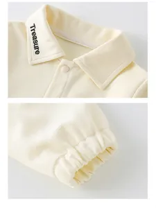 Close-up of beige corduroy baby top with Treasure embroidery and elastic cuffs