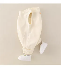 Detail der cremefarbenen Baby-Latzhose mit Bären-Aufnäher und passenden weißen Lauflernschuhen