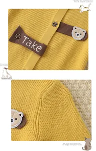 Detail of yellow knit baby romper featuring wooden buttons and cute bear embroidery