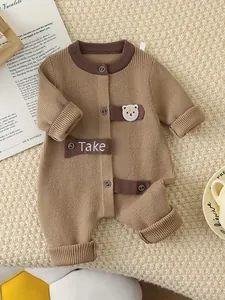 Brown knitted baby romper with bear embroidery and buttons on beige textured backdrop