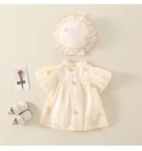 Dettaglio dell'abito da neonata color crema con ricamo a farfalla e cappellino