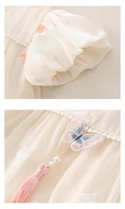 Dettaglio ricamo con perle e nappe lunghe su vestito pagliaccetto per neonata