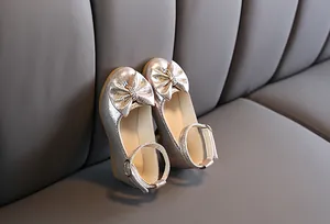 Close-up of champagne gold girls' princess shoes with glitter finish and rhinestone bow