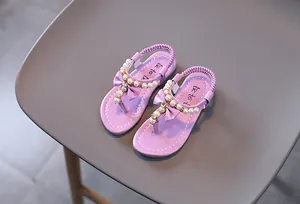 Detalle de sandalias moradas para niña con perlas elegantes y decoración de lazo