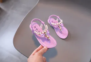 Detalle de sandalias moradas para niña con tiras de perlas y un lazo de seda decorativo