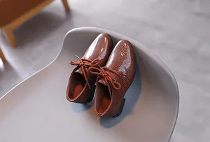 Nahaufnahme brauner Jungen-Lederschuhe mit Schlangenhautmuster und klassischen Schnürsenkeln
