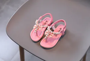 Detalle de sandalias rosas para niña con perlas artificiales y lazo de satén suave