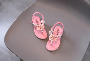 Detalle de sandalias rosas para niña con perlas, lazo y correa elástica en el talón